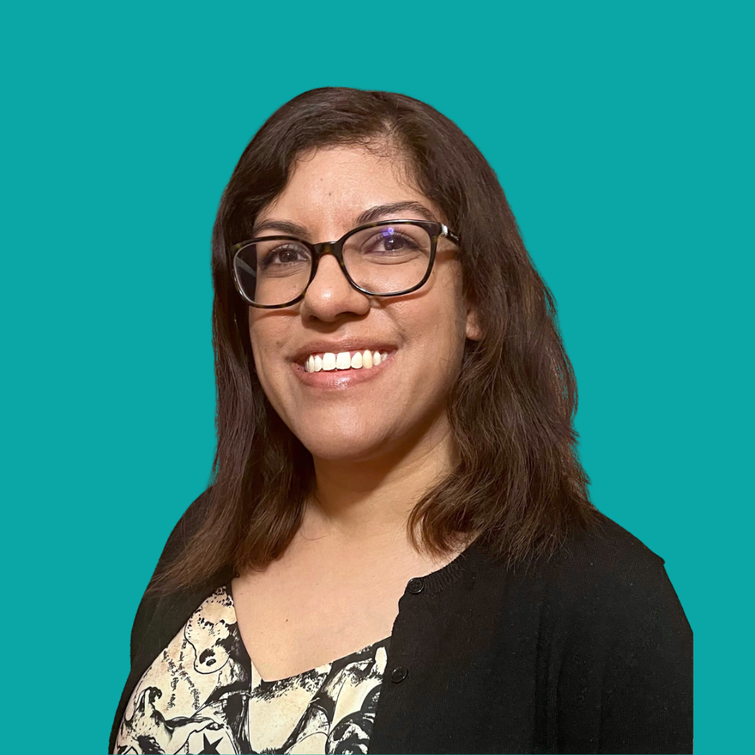 Headshot of Alana Sookoor, social worker and psychotherapist, smiling against a teal background, wearing glasses and a tan & black blouse